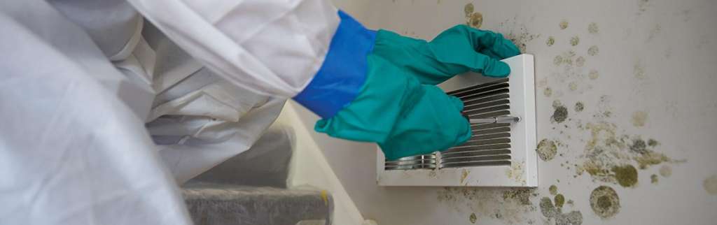Worker in hazmat suit removing vent from moldy wall